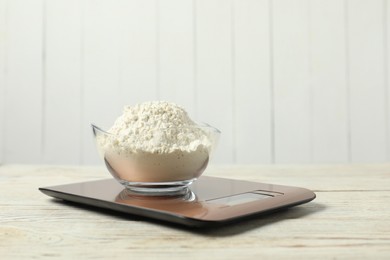 Photo of Modern electronic kitchen scale with bowl of flour on wooden table