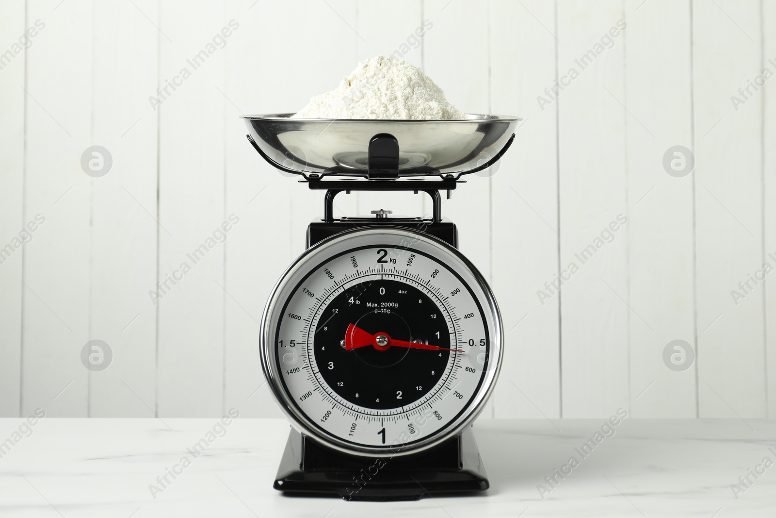 Photo of Retro mechanical kitchen scale with flour on white marble table