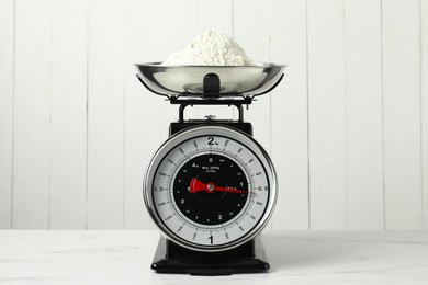 Photo of Retro mechanical kitchen scale with flour on white marble table