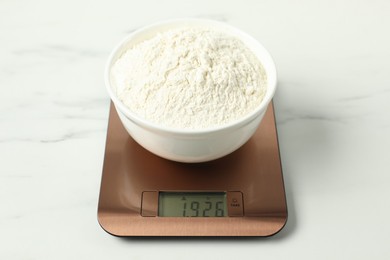 Photo of Modern electronic kitchen scale with bowl of flour on white marble table, closeup