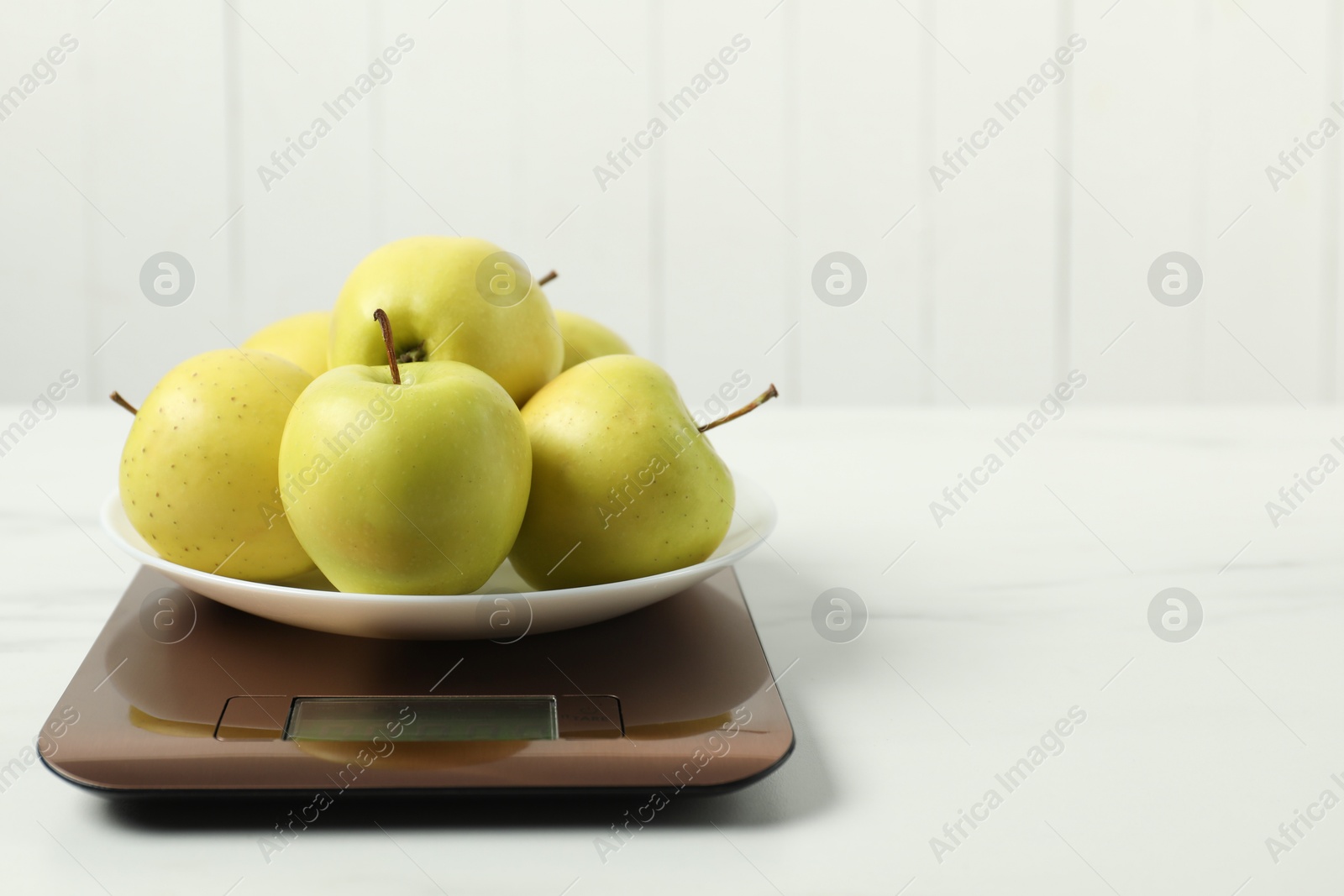 Photo of Modern electronic kitchen scale with apples on white marble table. Space for text