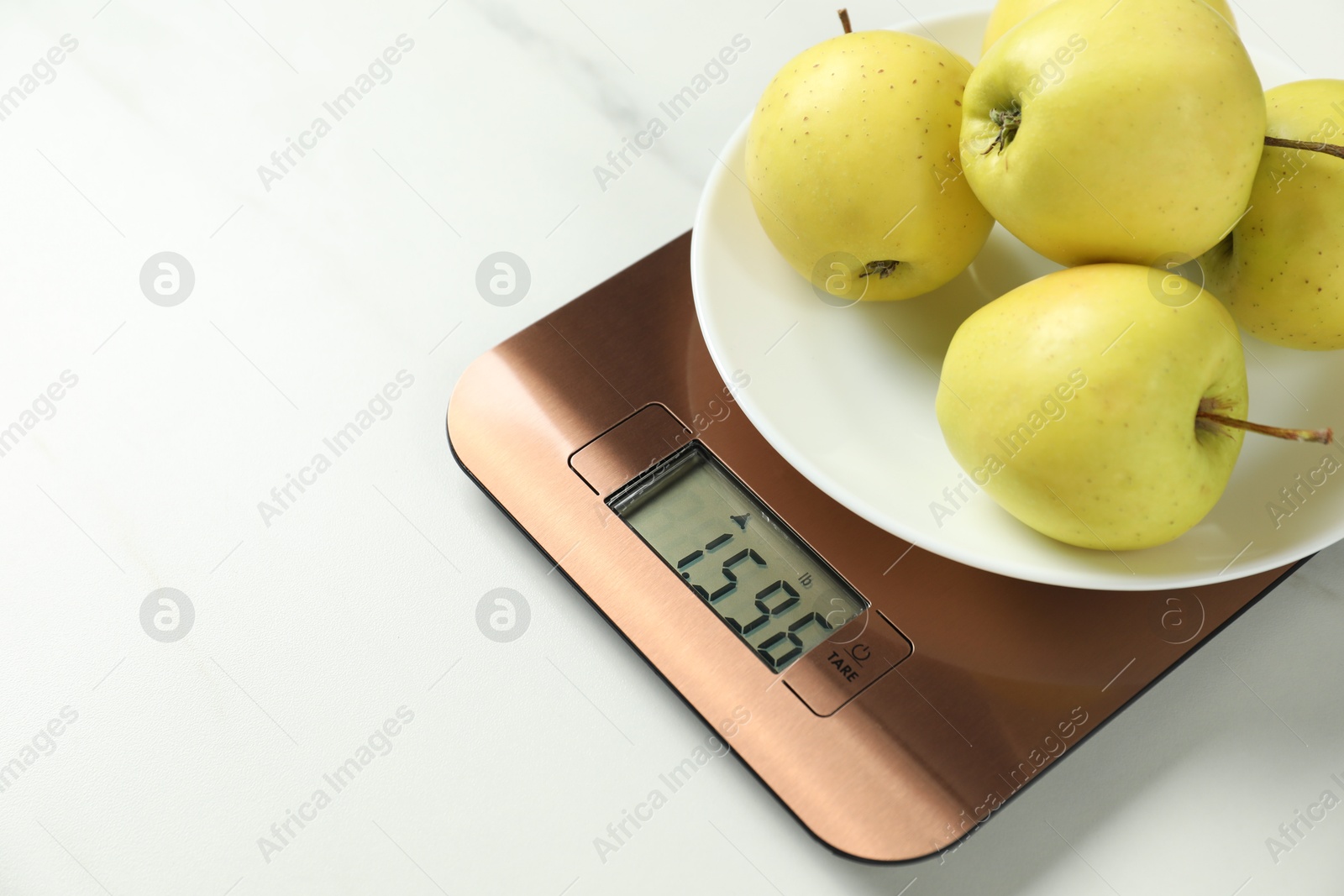 Photo of Modern electronic kitchen scale with apples on white marble table, closeup. Space for text