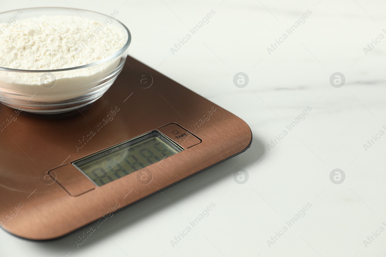 Photo of Modern electronic kitchen scale with bowl of flour on white marble table, closeup. Space for text