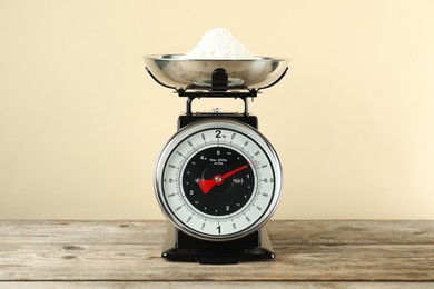 Photo of Mechanical kitchen scale with bowl of flour on wooden table against beige background