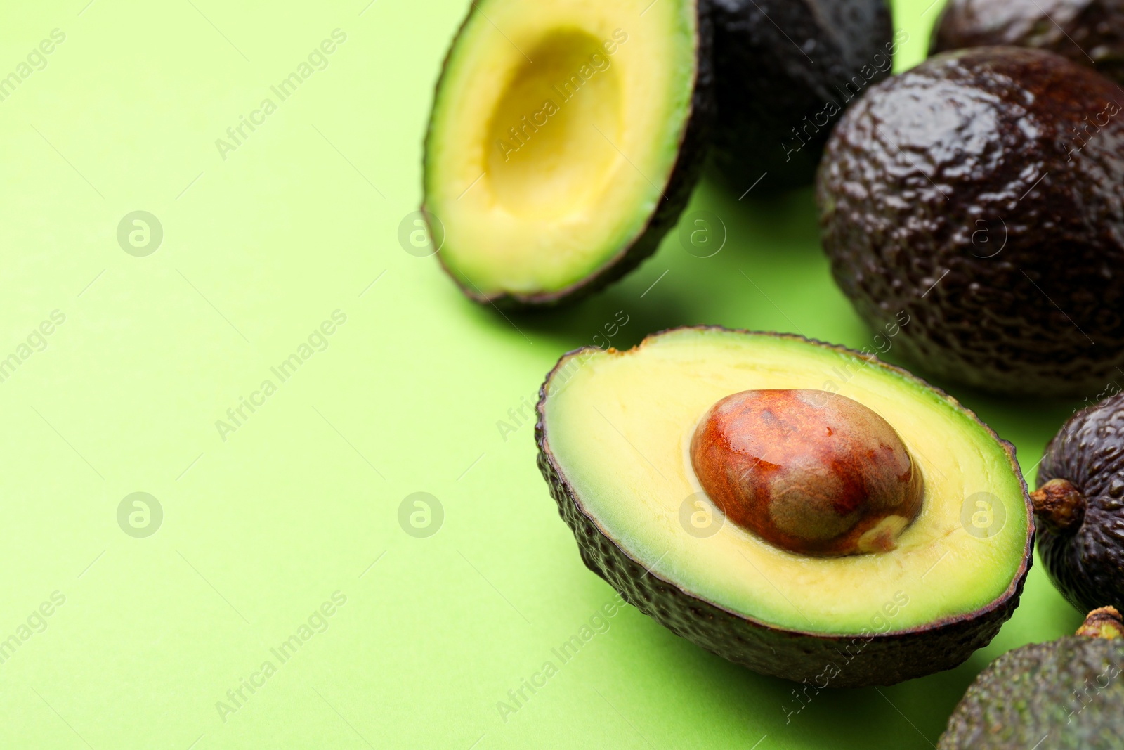 Photo of Fresh ripe avocados on light green background, closeup. Space for text