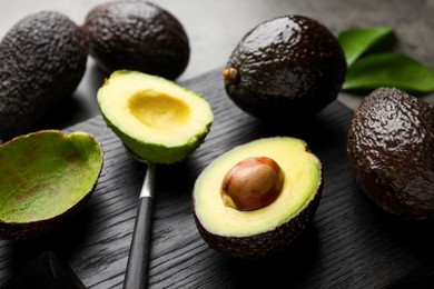 Photo of Fresh ripe avocados, spoon and leaves on grey table, closeup