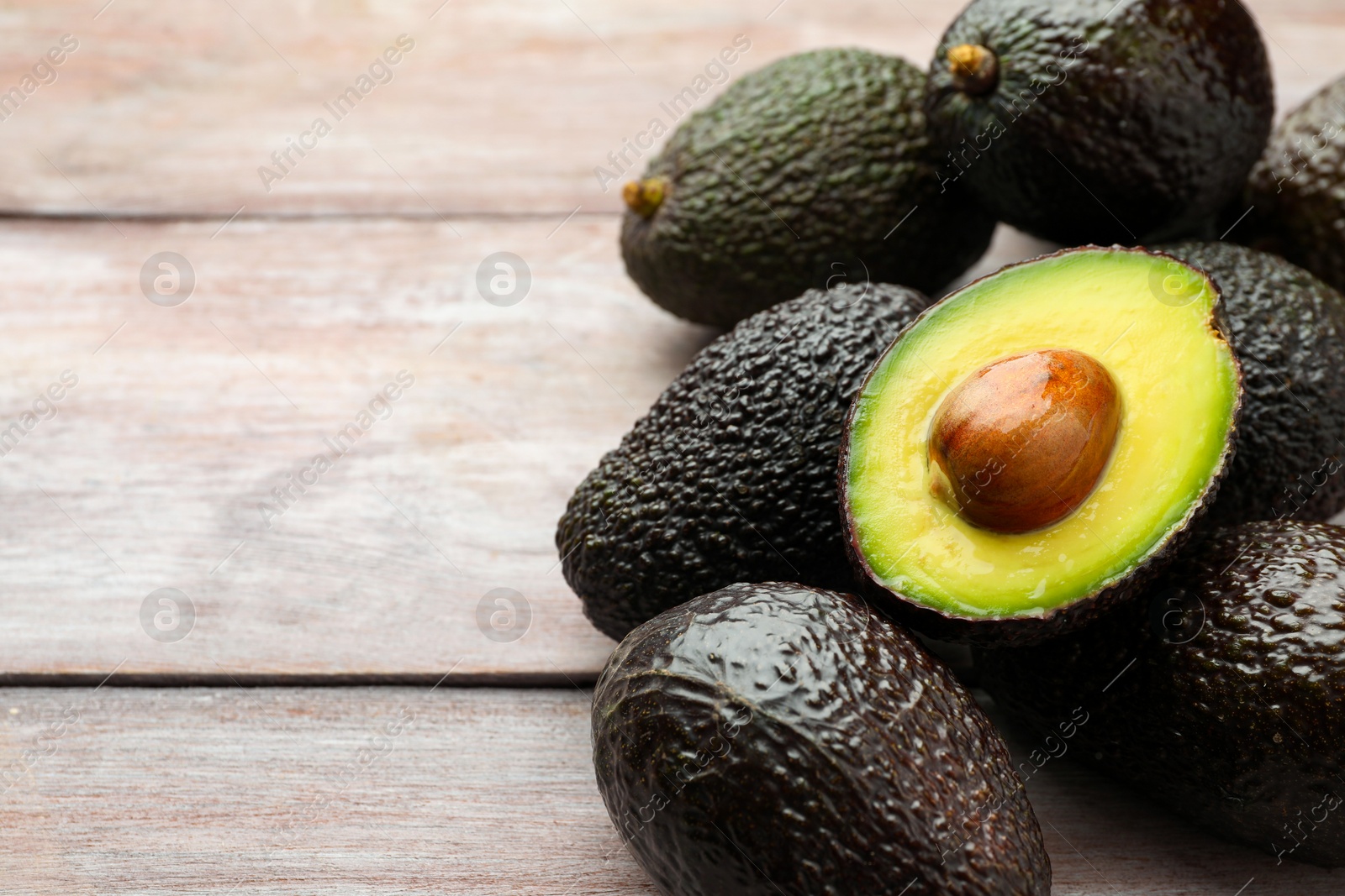 Photo of Fresh ripe avocados on light wooden table, closeup. Space for text