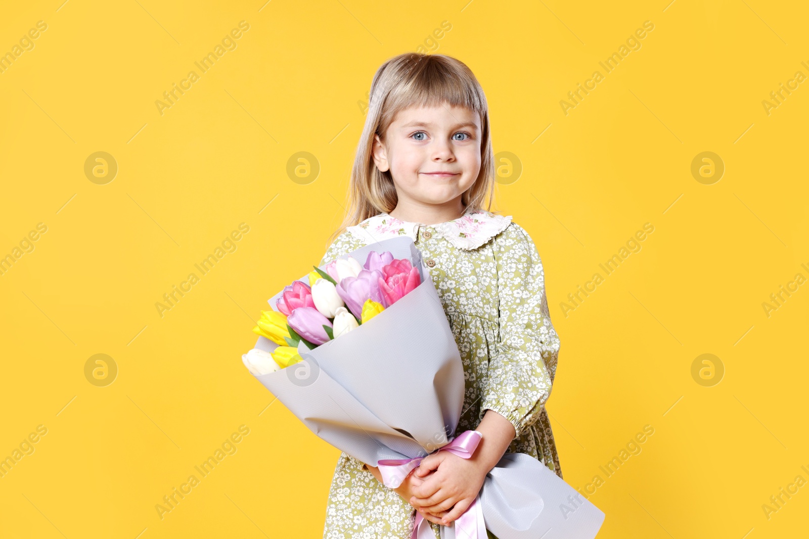 Photo of Cute little girl with bouquet of tulips on orange background