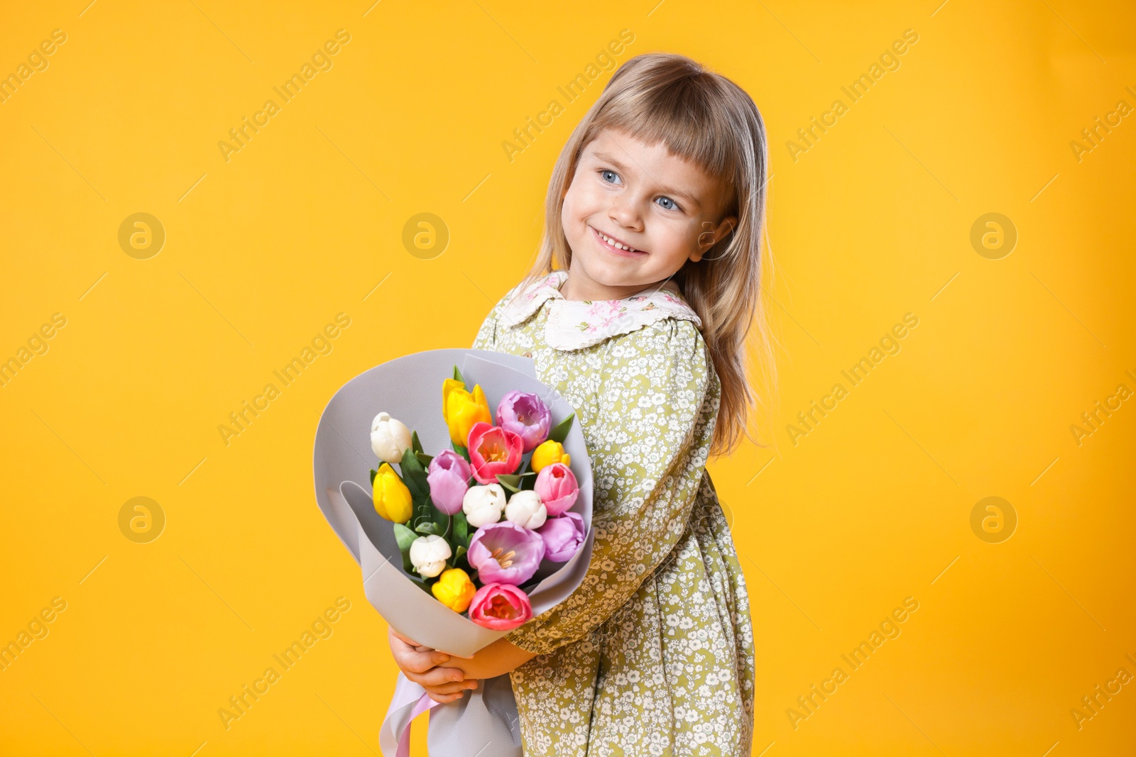 Photo of Smiling little girl with bouquet of tulips on orange background