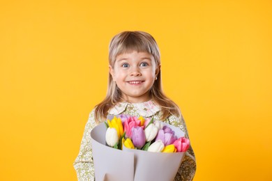 Photo of Smiling little girl with bouquet of tulips on orange background