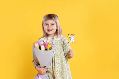 Photo of Smiling little girl with bouquet of tulips and decorative Easter bunny on orange background