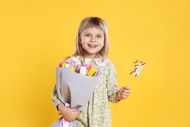 Photo of Smiling little girl with bouquet of tulips and decorative Easter bunny on orange background