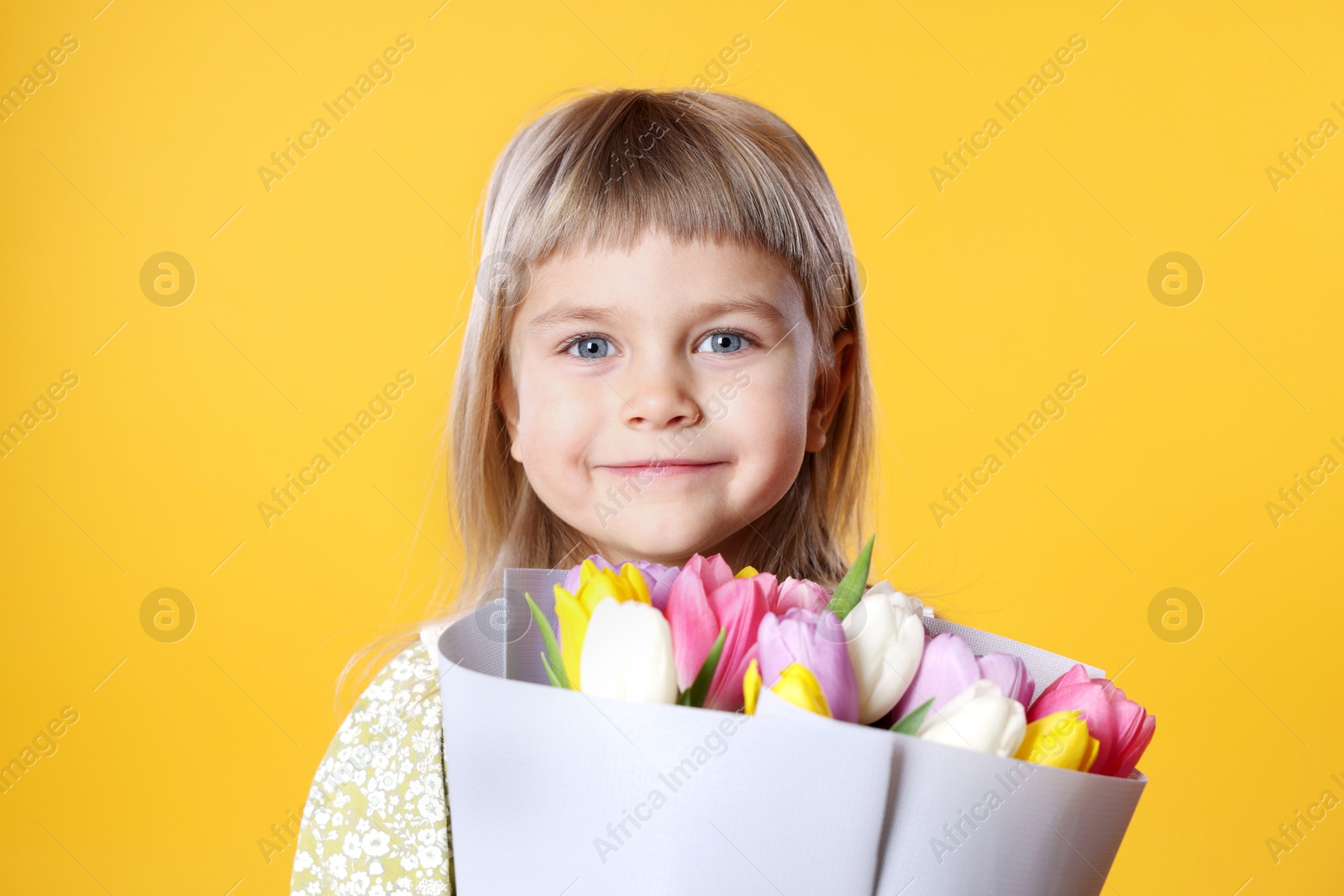 Photo of Cute little girl with bouquet of tulips on orange background