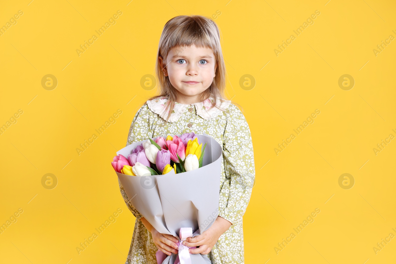 Photo of Cute little girl with bouquet of tulips on orange background