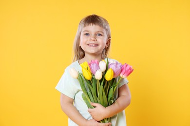 Smiling little girl with bouquet of tulips on yellow background