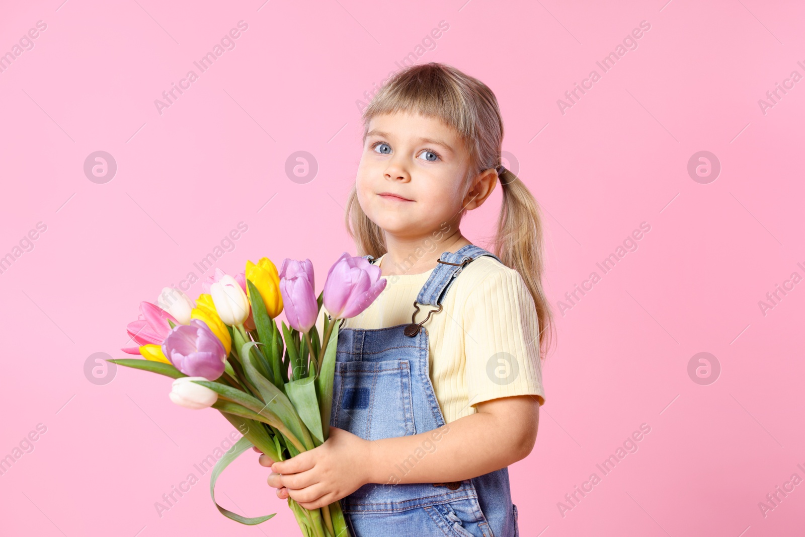 Photo of Cute little girl with bouquet of tulips on pink background