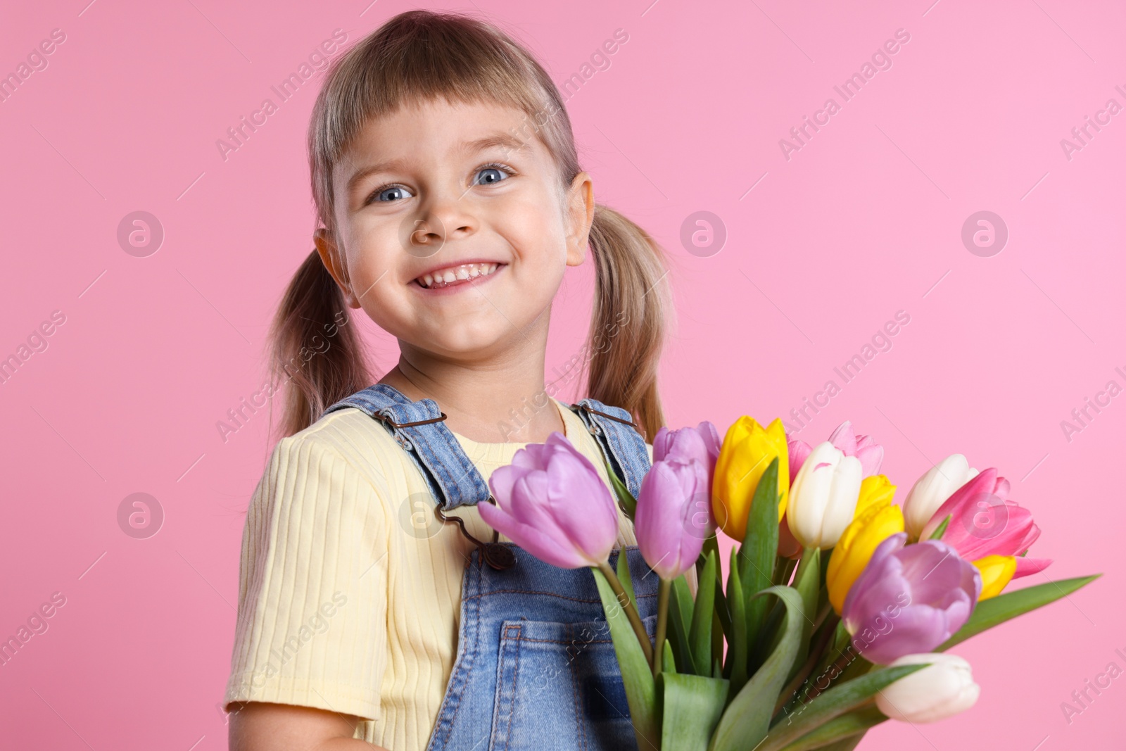 Photo of Smiling little girl with bouquet of tulips on pink background