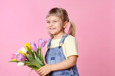 Photo of Smiling little girl with bouquet of tulips on pink background