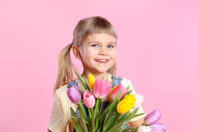 Photo of Smiling little girl with bouquet of tulips on pink background