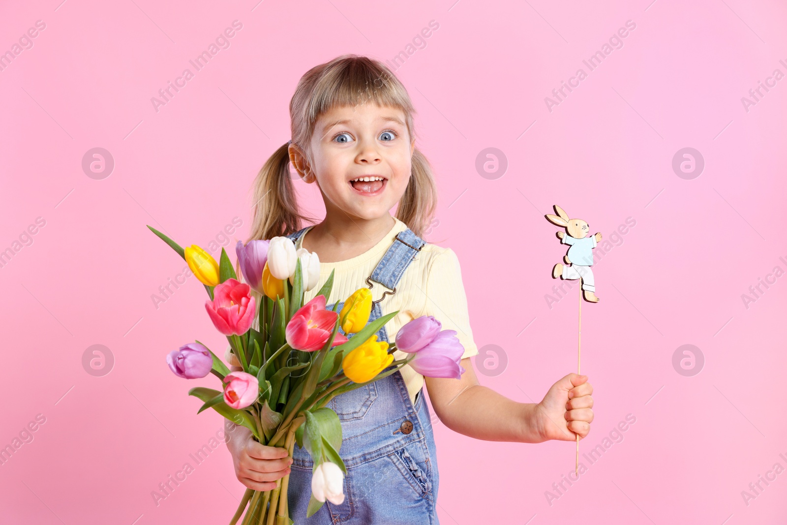 Photo of Happy little girl with bouquet of tulips and decorative Easter bunny on pink background