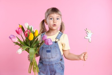 Photo of Cute little girl with bouquet of tulips and decorative Easter bunny on pink background