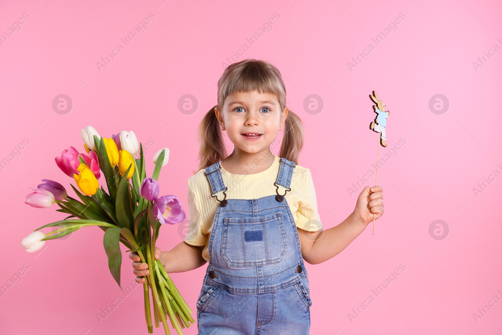 Photo of Smiling little girl with bouquet of tulips and decorative Easter bunny on pink background