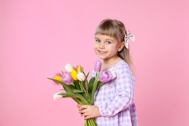 Photo of Smiling little girl with bouquet of tulips on pink background. Space for text