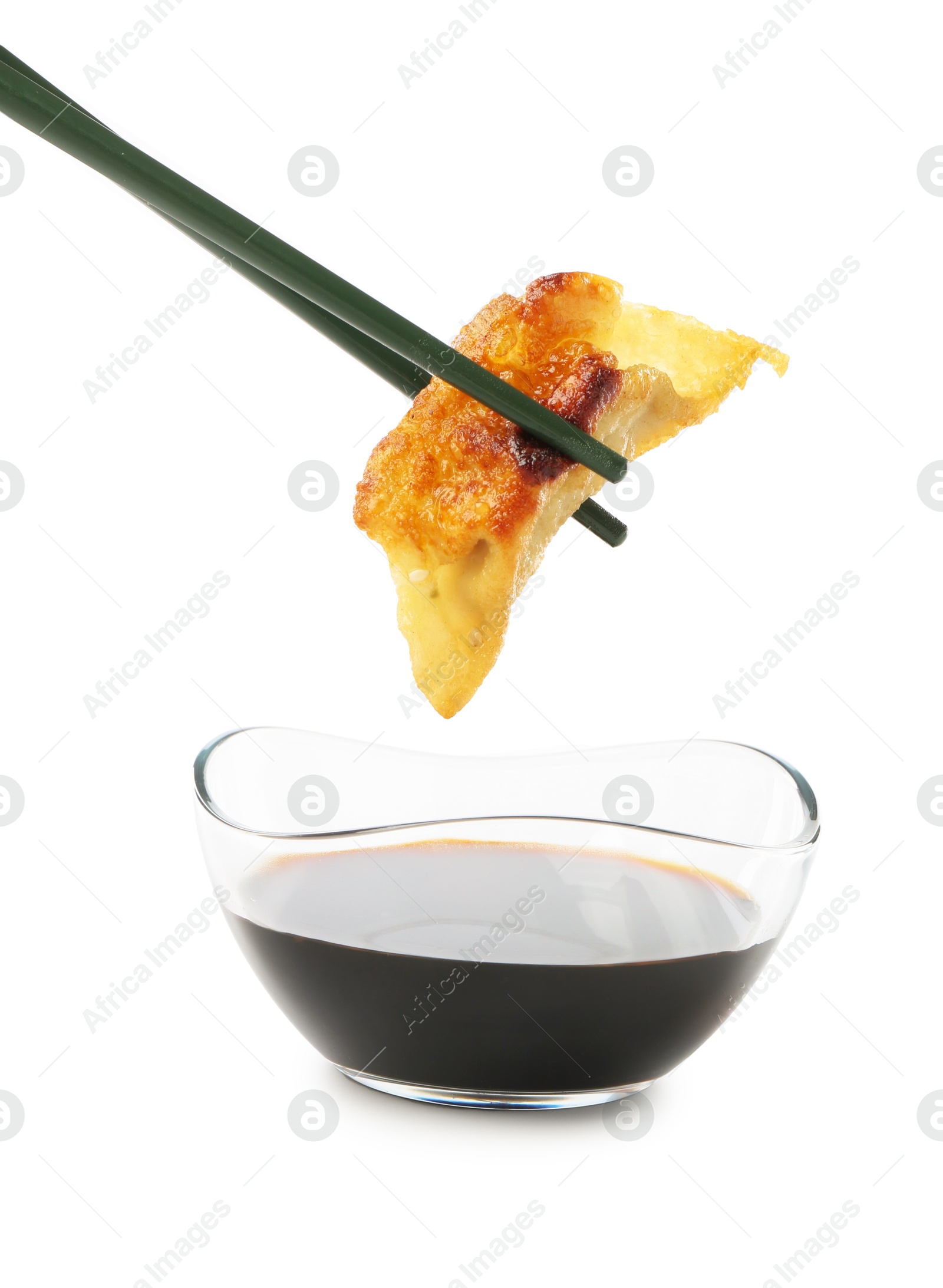 Photo of Dipping tasty fried gyoza (dumpling) into soy sauce on white background