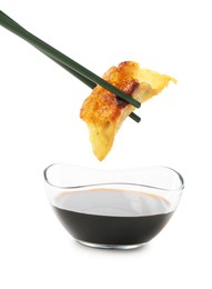 Photo of Dipping tasty fried gyoza (dumpling) into soy sauce on white background