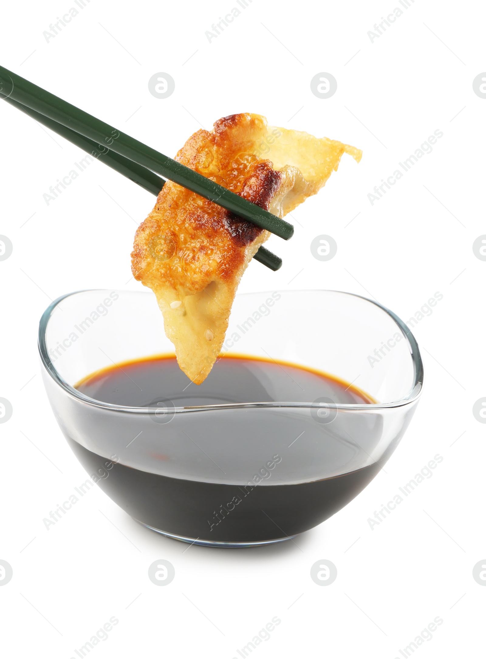 Photo of Dipping tasty fried gyoza (dumpling) into soy sauce on white background