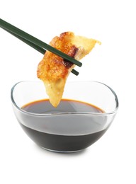 Photo of Dipping tasty fried gyoza (dumpling) into soy sauce on white background