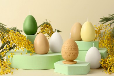 Photo of Beautiful egg shaped candles and mimosa flowers on beige background. Easter decor