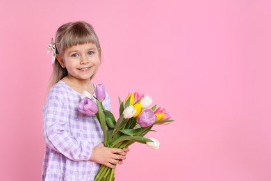 Photo of Smiling little girl with bouquet of tulips on pink background. Space for text