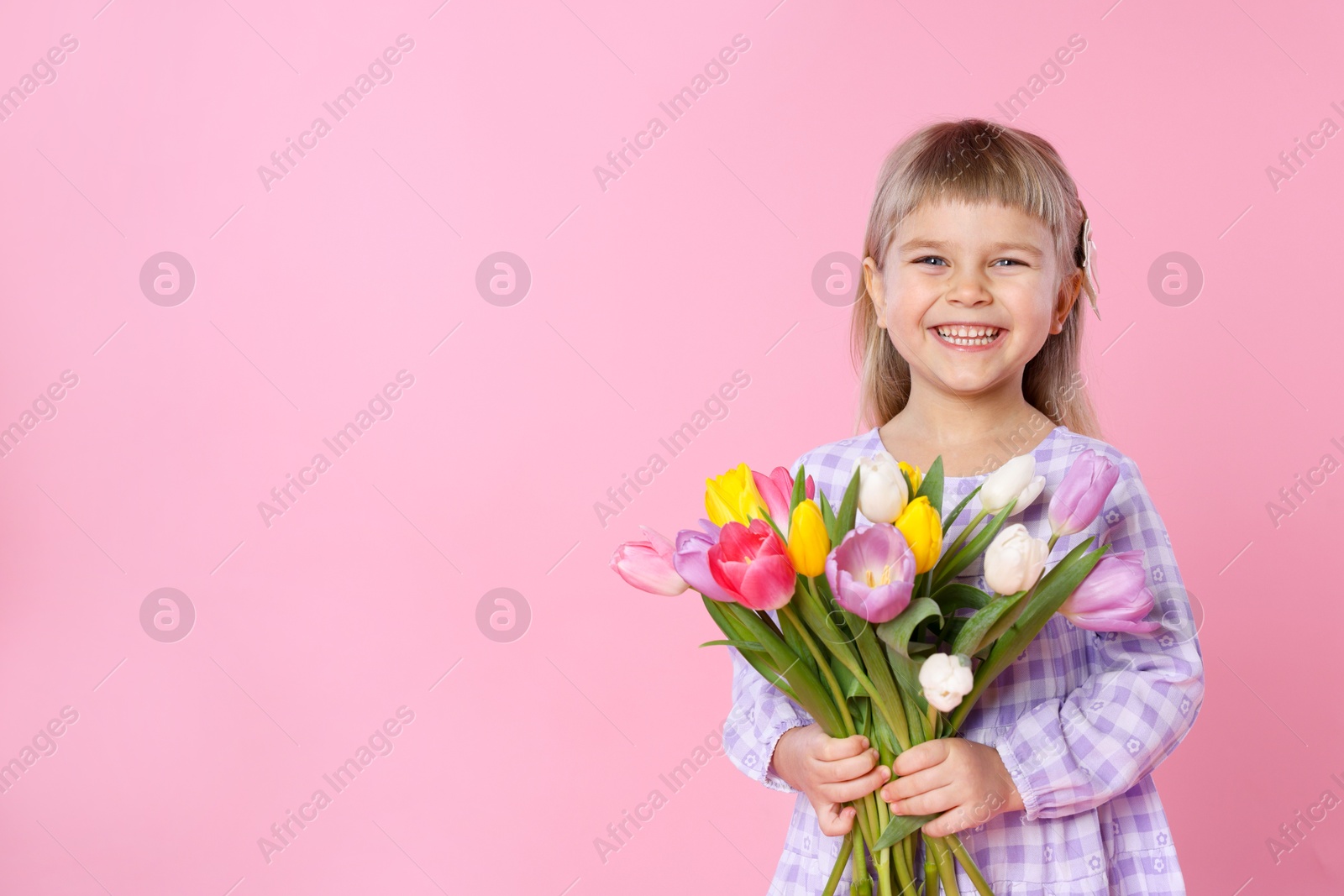 Photo of Smiling little girl with bouquet of tulips on pink background. Space for text