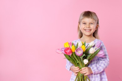 Photo of Smiling little girl with bouquet of tulips on pink background. Space for text