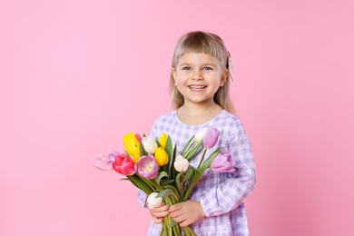 Photo of Smiling little girl with bouquet of tulips on pink background. Space for text