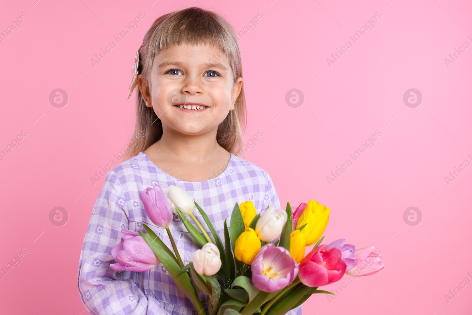 Photo of Smiling little girl with bouquet of tulips on pink background