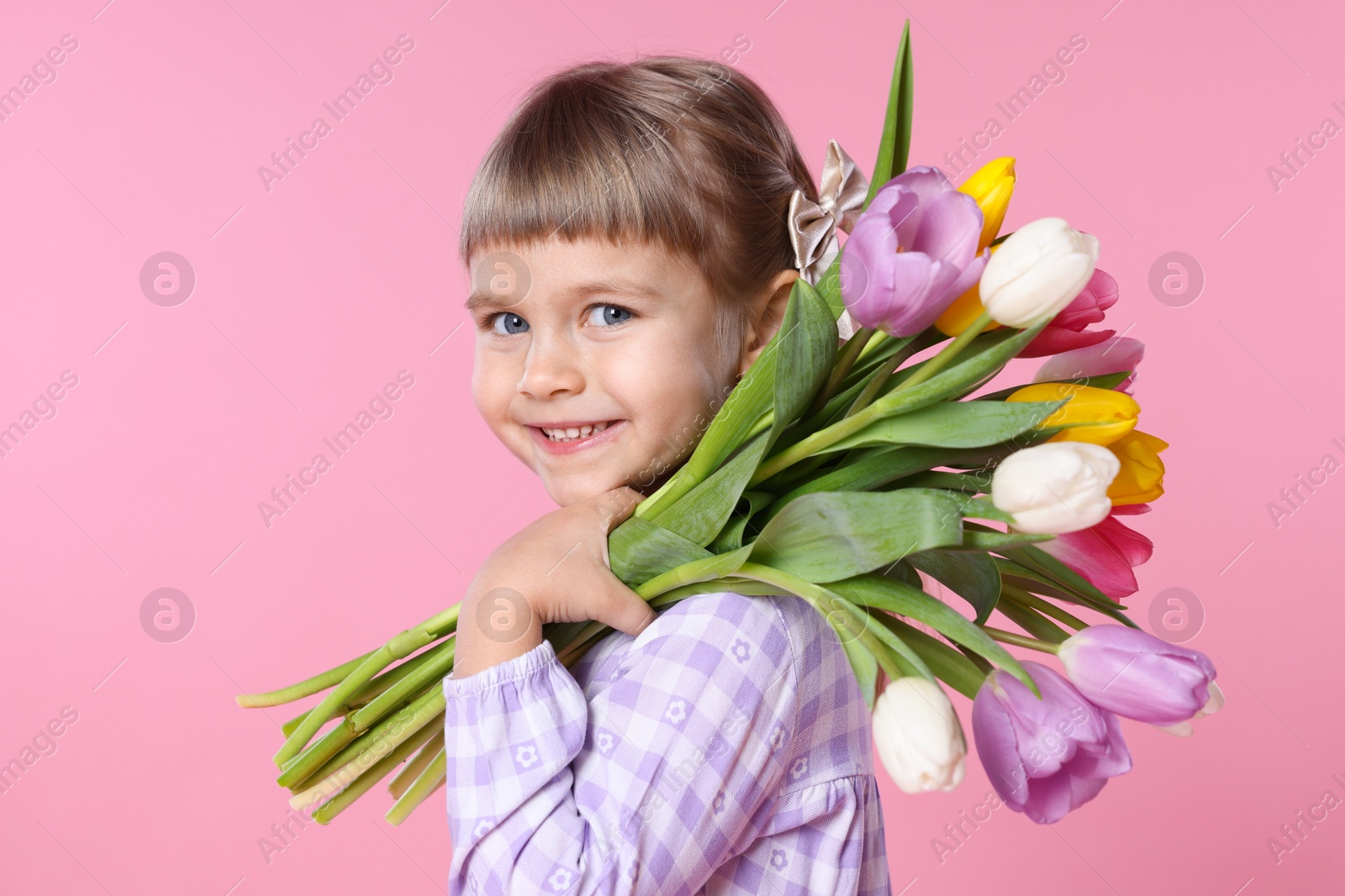 Photo of Smiling little girl with bouquet of tulips on pink background