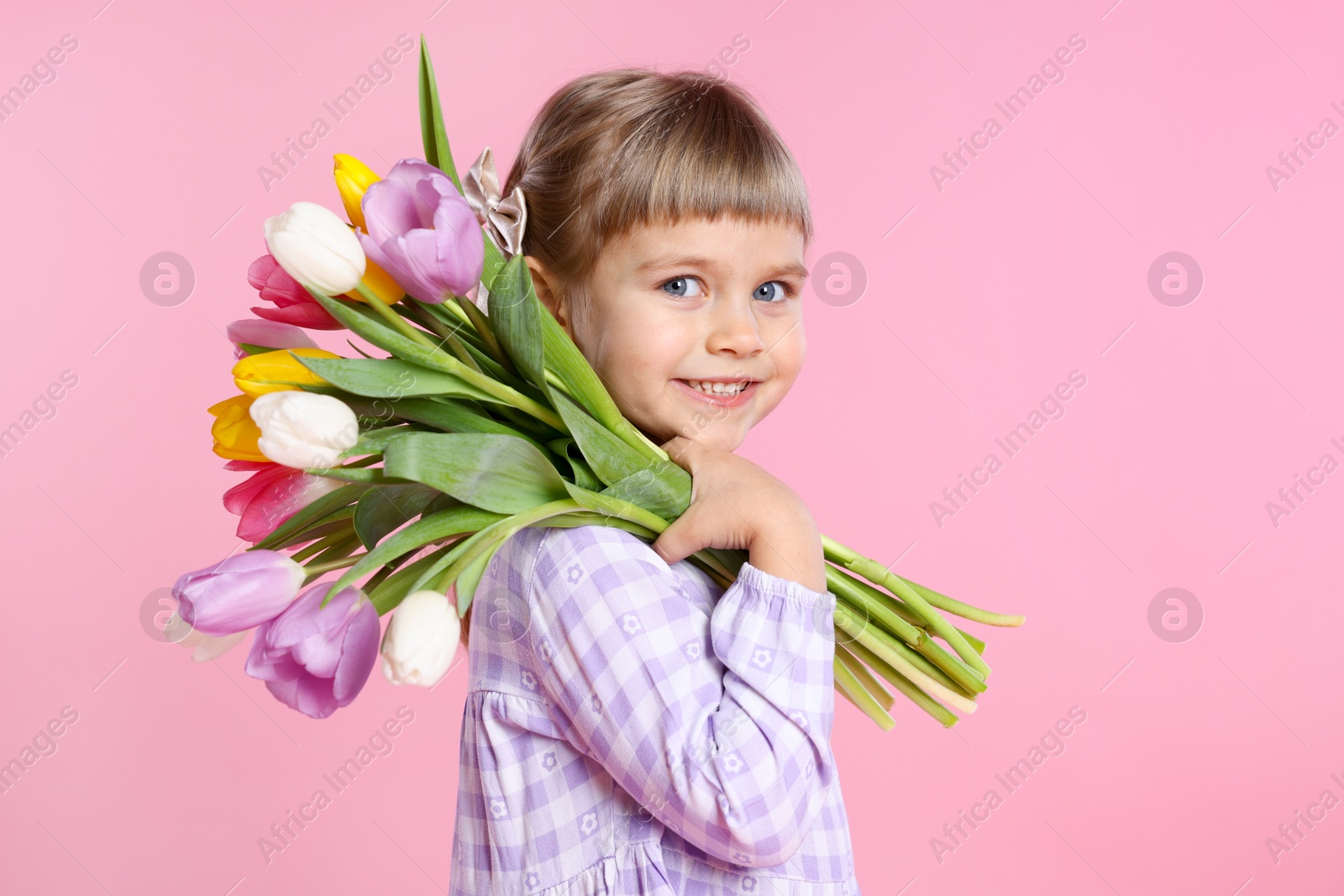 Photo of Smiling little girl with bouquet of tulips on pink background