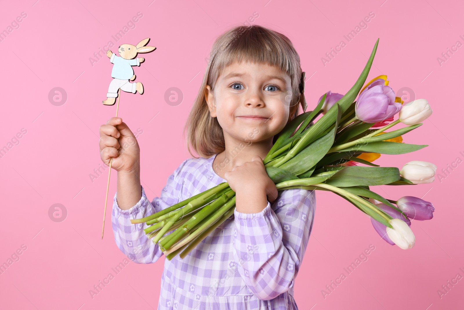 Photo of Cute little girl with bouquet of tulips and decorative Easter bunny on pink background