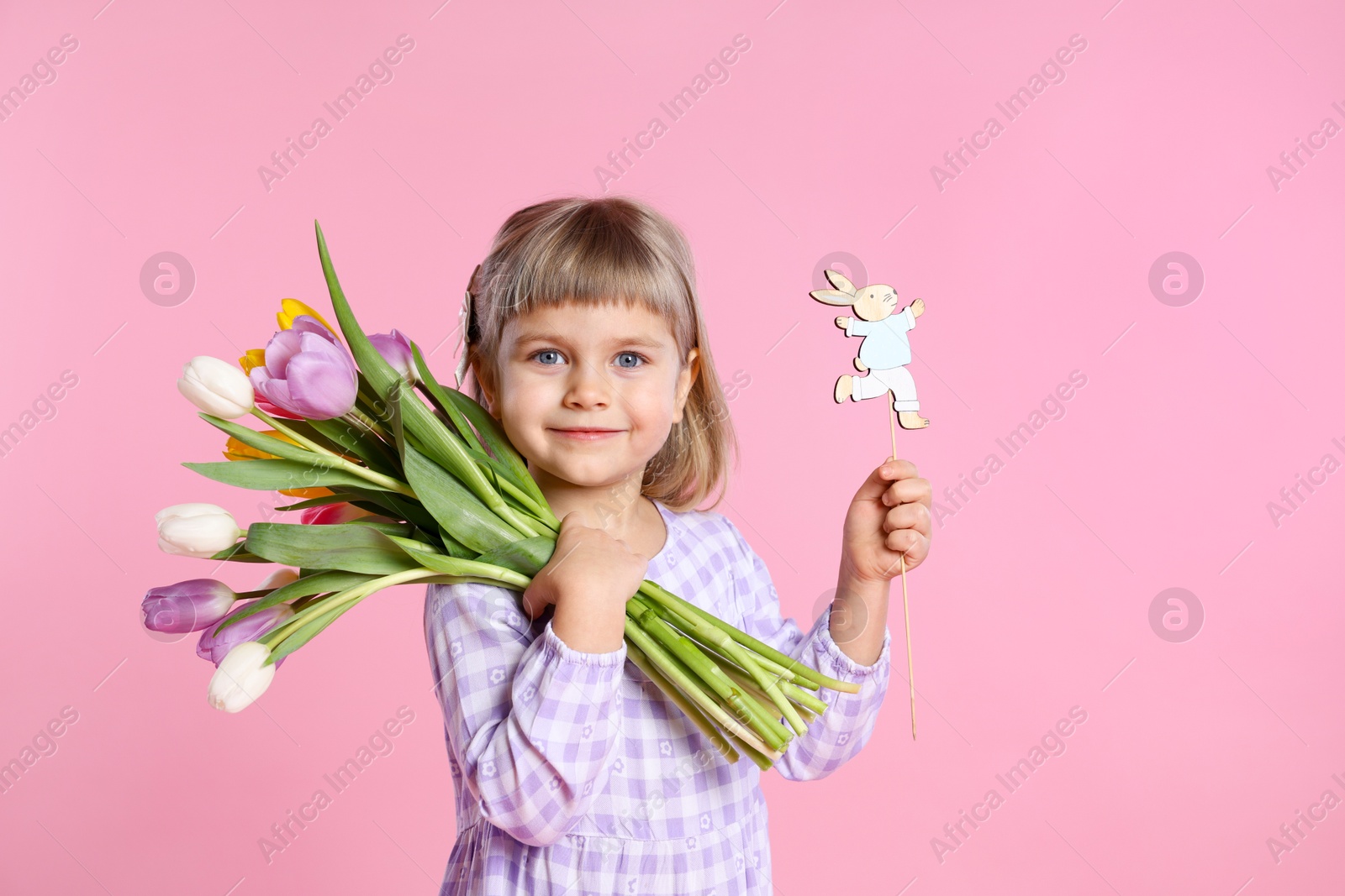 Photo of Cute little girl with bouquet of tulips and decorative Easter bunny on pink background