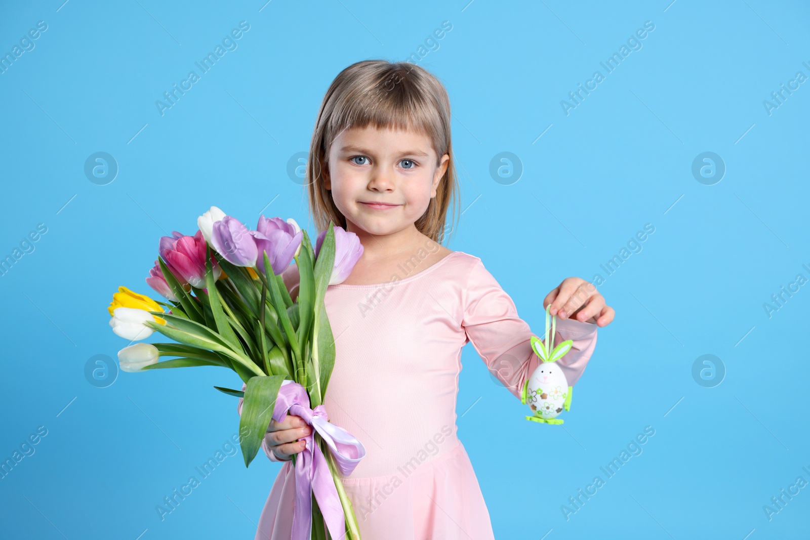 Photo of Cute little girl with bouquet of tulips and decorative Easter egg on light blue background