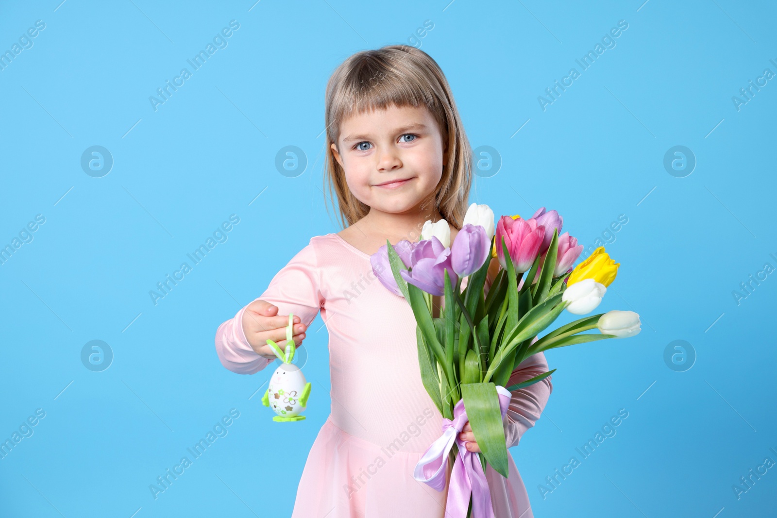 Photo of Cute little girl with bouquet of tulips and decorative Easter egg on light blue background