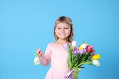 Photo of Smiling little girl with bouquet of tulips and decorative Easter egg on light blue background