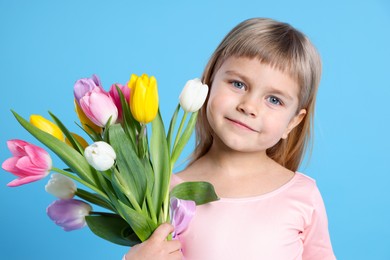 Photo of Cute little girl with bouquet of tulips on light blue background