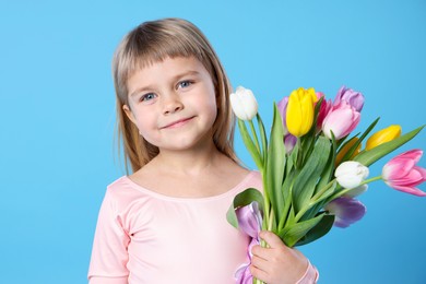 Cute little girl with bouquet of tulips on light blue background