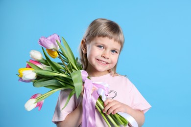 Photo of Smiling little girl with bouquet of tulips on light blue background