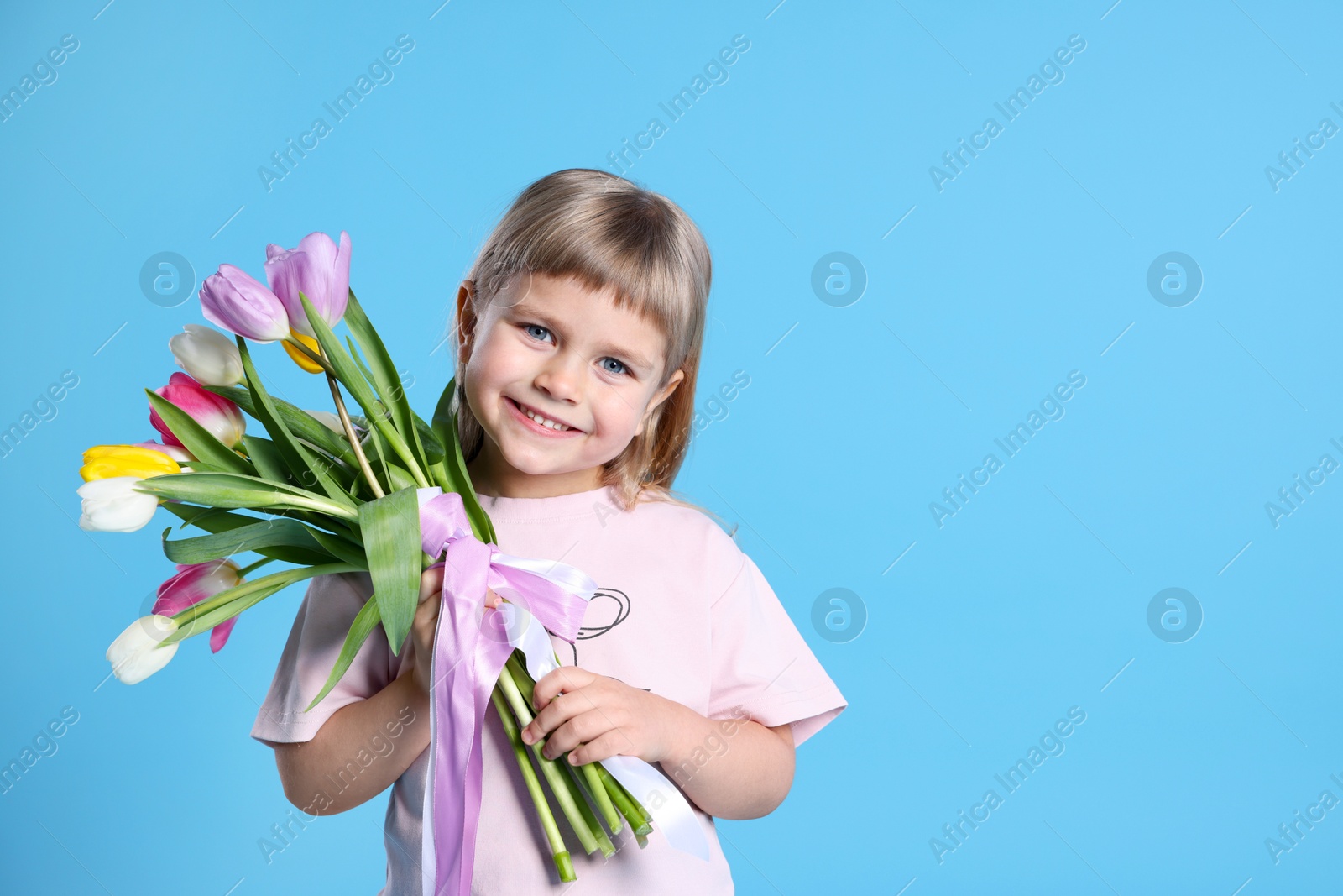 Photo of Smiling little girl with bouquet of tulips on light blue background. Space for text