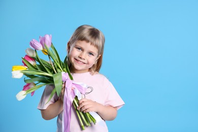 Photo of Smiling little girl with bouquet of tulips on light blue background. Space for text