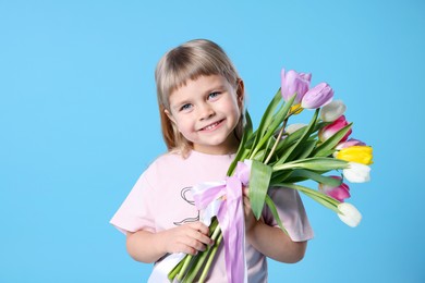 Photo of Smiling little girl with bouquet of tulips on light blue background